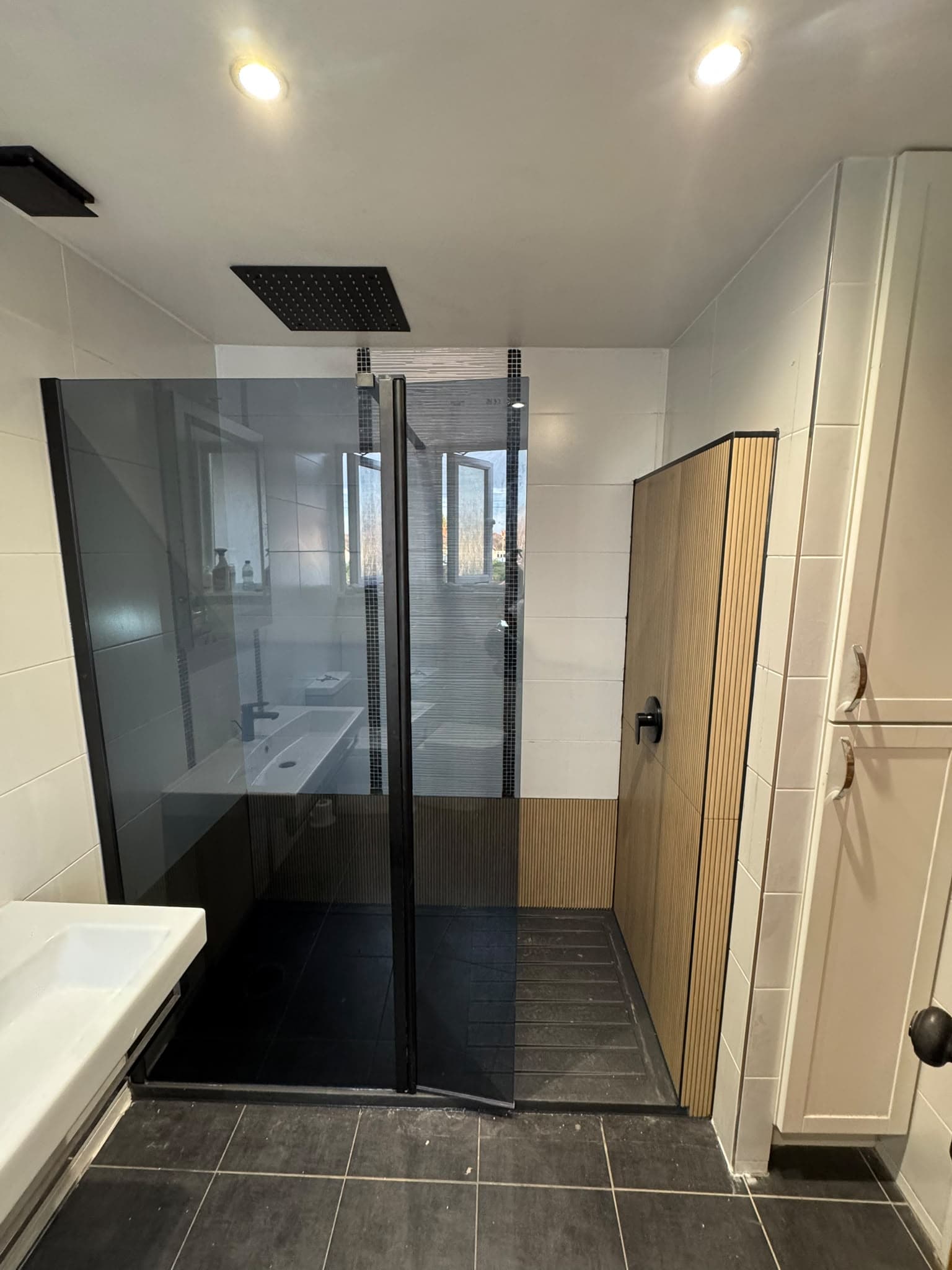 Bath to walk-in shower conversion: black-framed smoked glass screen, ceiling rainfall shower and wood-effect fluted tiles